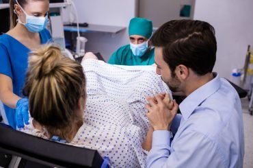 Medical team examining pregnant woman during delivery while man holding her hand in operating room