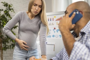 pregnant-businesswoman-labour-male-coworker-calling-emergency-service